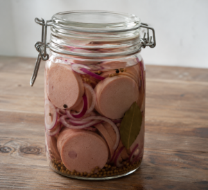 Traditionele flauwekul (leverworst) in een glazen weckpot met rode ui en kruiden op een houten tafel.